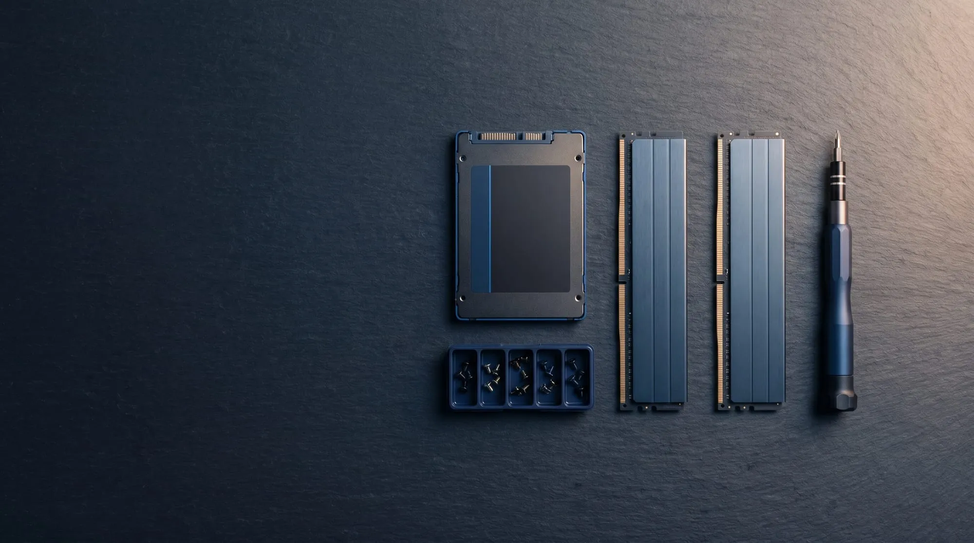 Strakke flat-lay van een SSD, geheugenmodules en gesorteerde schroefjes op een donkere ondergrond
